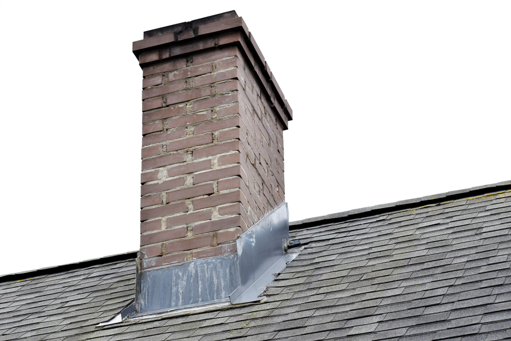 Brown brick chimney on grey asphalt shingles roof against sky